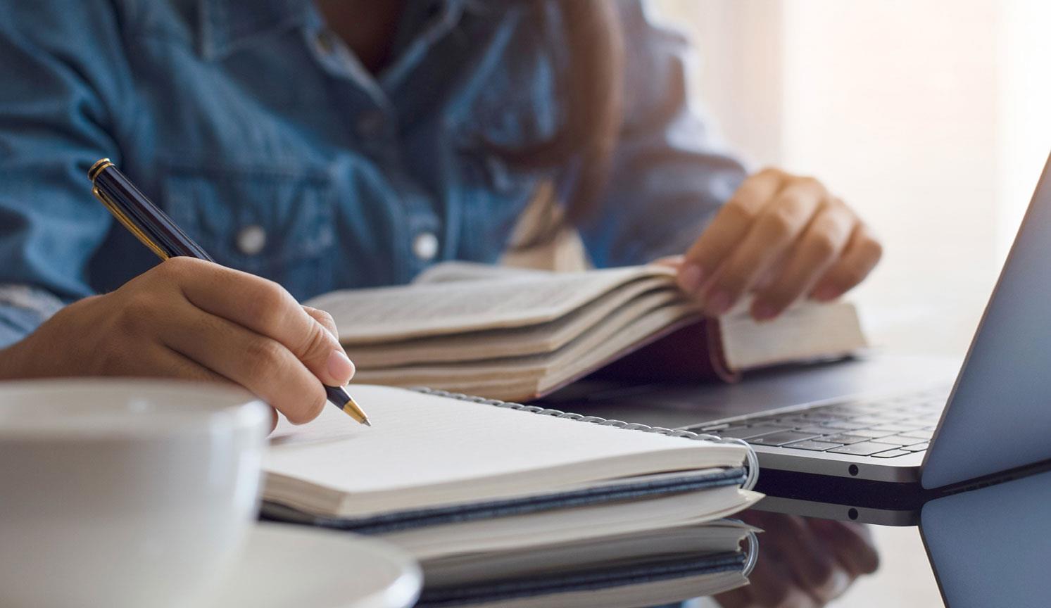 close up of person taking notes from reference book and computer
